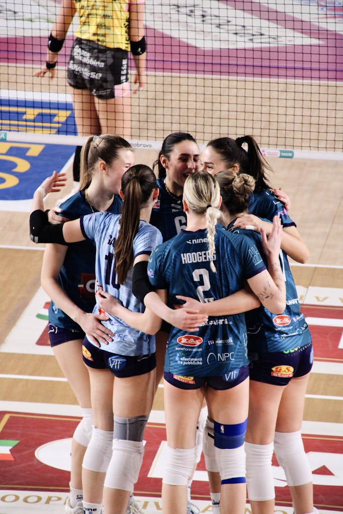A group of female volleyball players celebrate on the court after scoring a point.