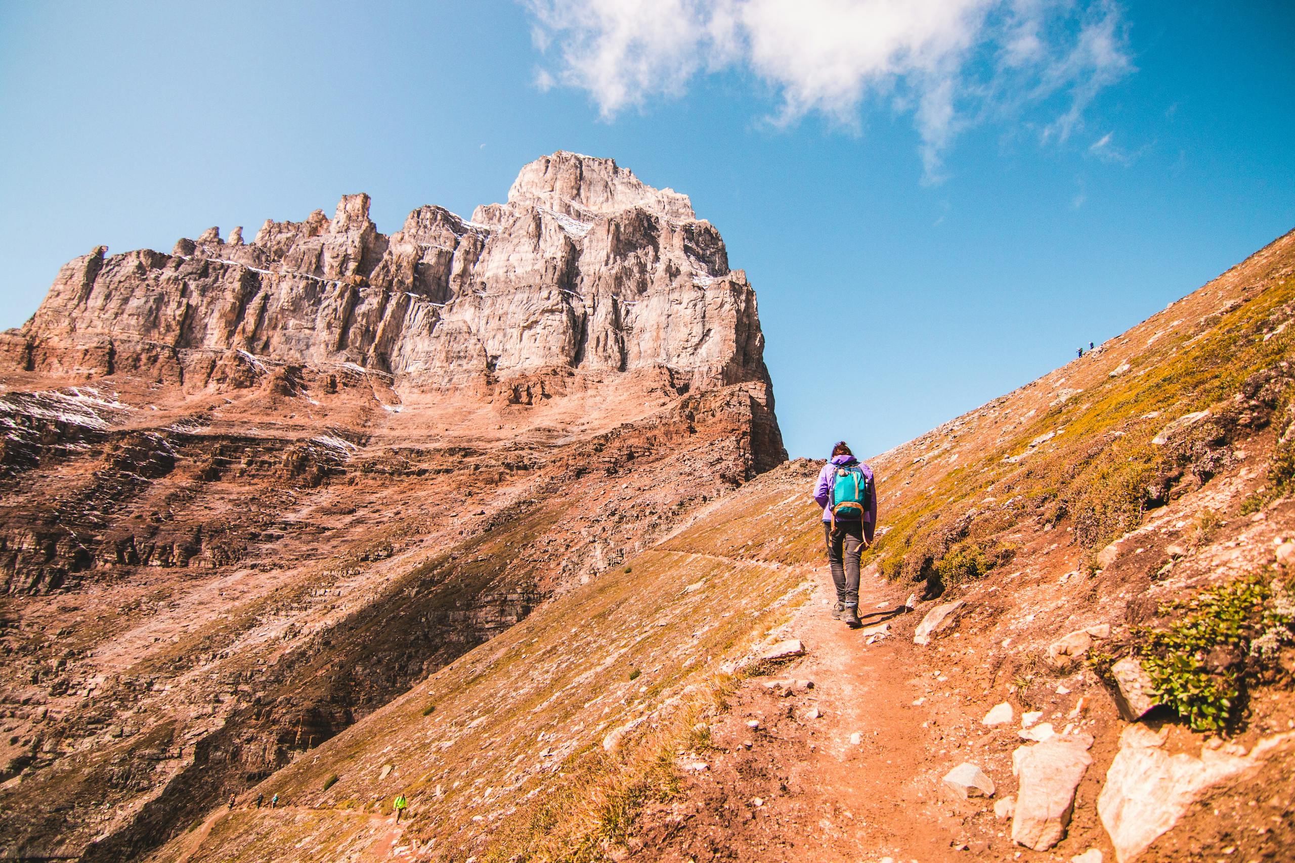 Person hiking towards dramatic rock formations in Banff, Canada, under a clear blue sky.
