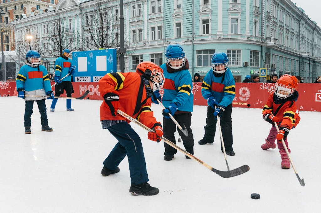 Kids in colorful gear playing ice hockey outdoors on a winter day.