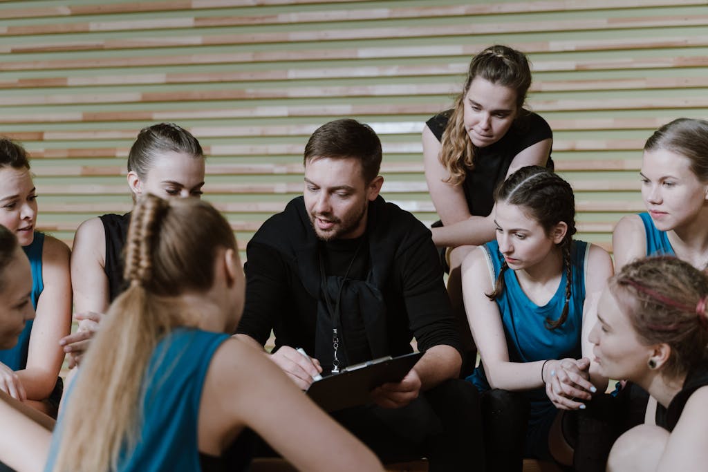 A coach discusses strategy with a women's team seated in a gym setting.