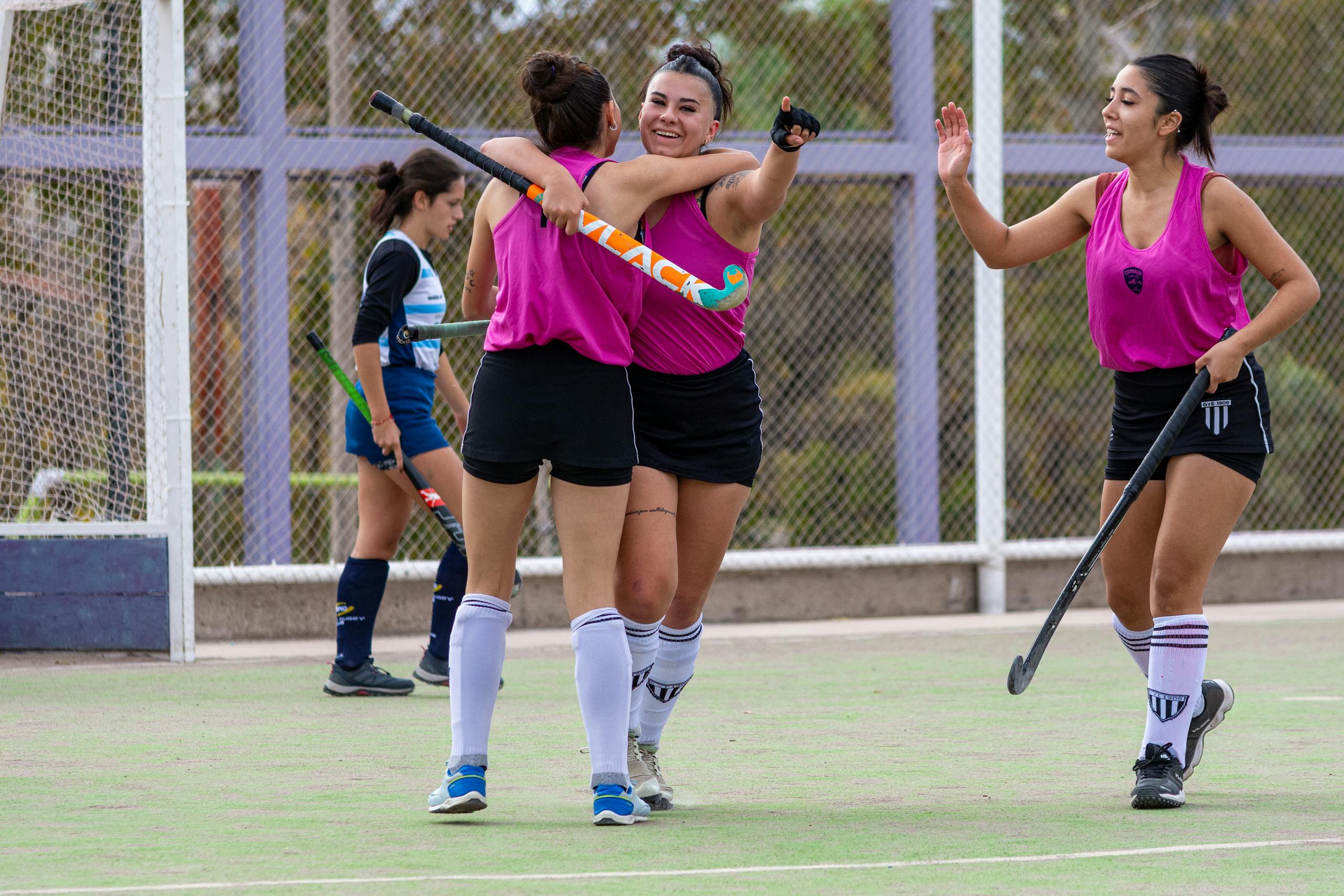 Female field hockey players celebrating a successful goal during a match.